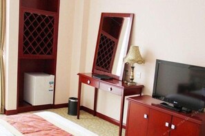 Une chambre d’hôtel équipée d’un lit, d’un bureau avec un ordinateur, d’une télévision, d’une armoire et d’un petit réfrigérateur.