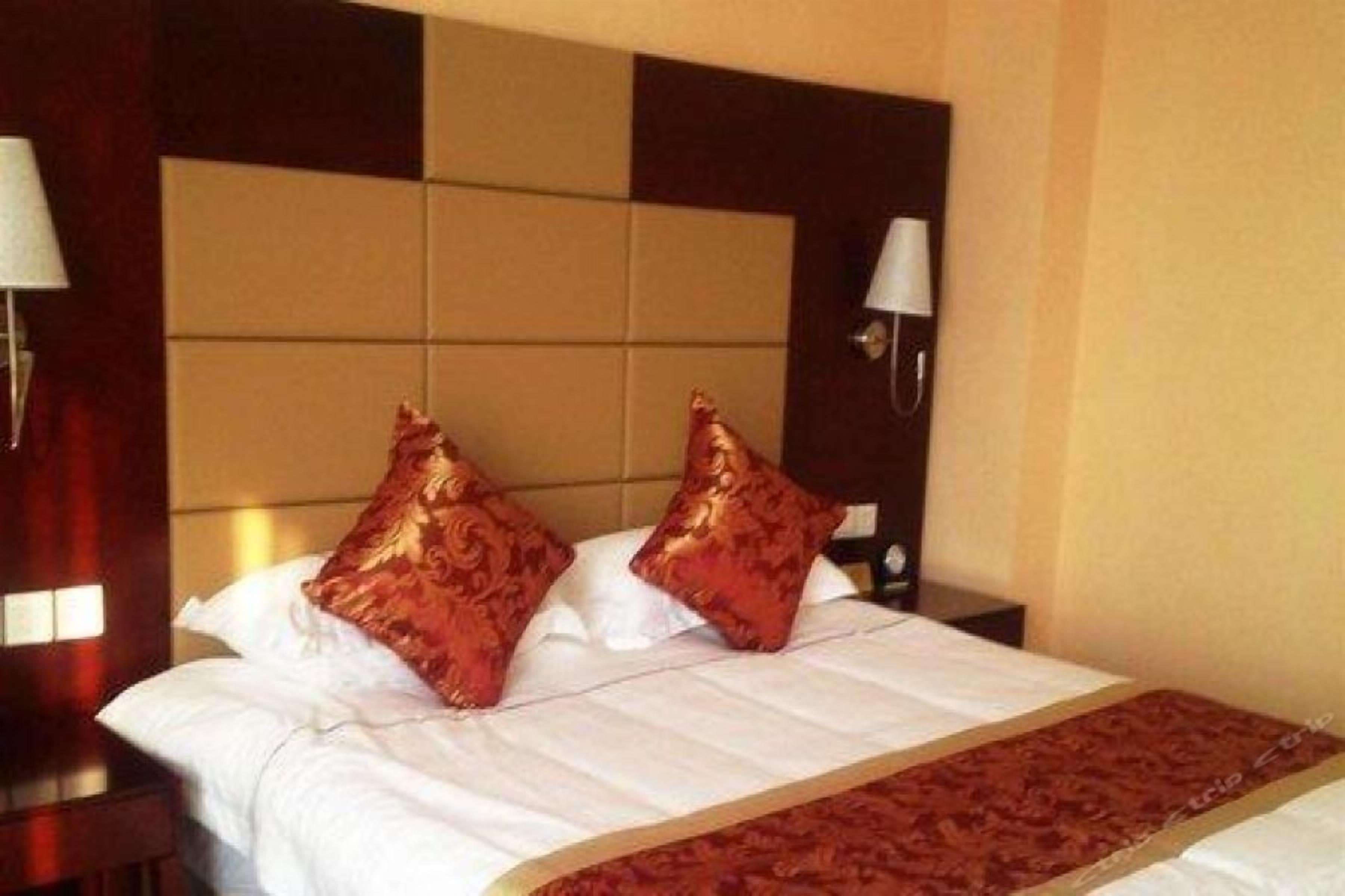 Una habitación de hotel con una cama, dos almohadas, una mesita de noche, una lámpara y un aplique de pared.