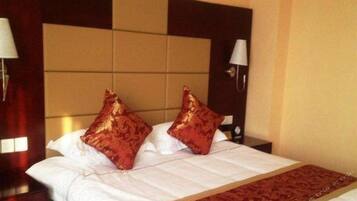 Una habitación de hotel con una cama, dos almohadas, una mesita de noche, una lámpara y un aplique de pared.