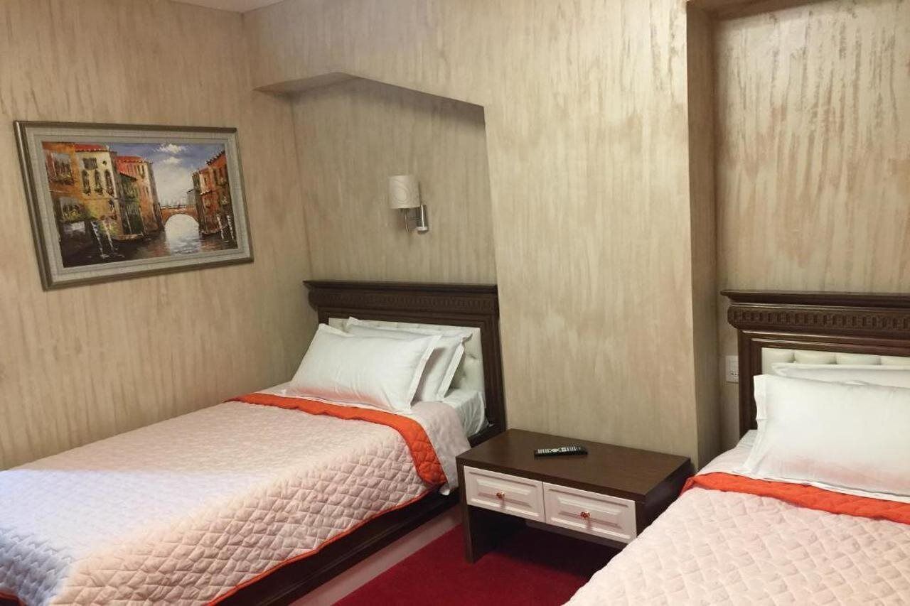 Hotellihuone, jossa on kaksi sänkyä, maalaus, jossa on kuvattuna kanava, yöpöytä ja lamppu.