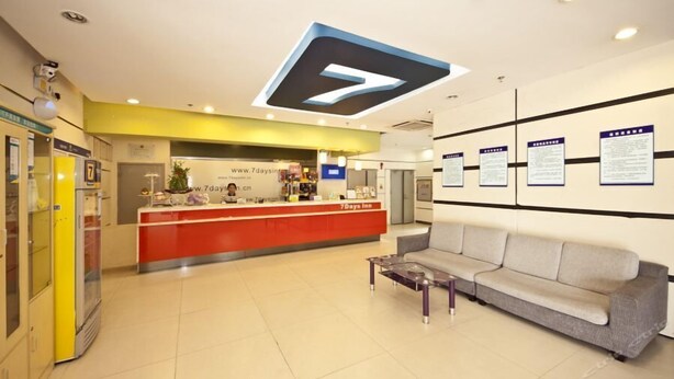 A hotel reception area with a red counter, a sofa, and informational posters on the wall.