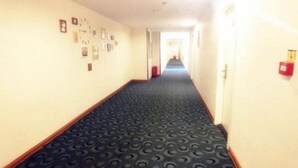 A hotel hallway with a patterned carpet, framed pictures on the wall, and a fire alarm on the right.