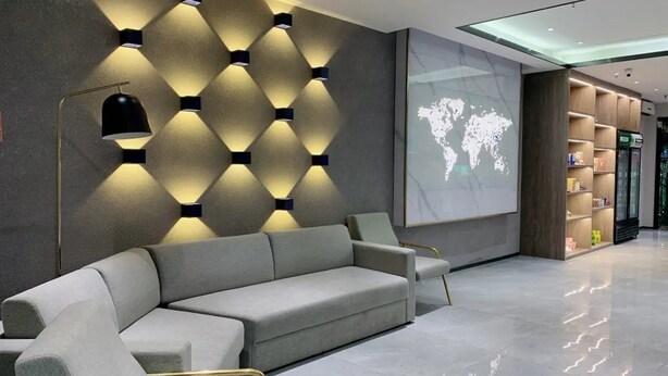 Un hall d’entrée moderne avec un canapé gris, un luminaire fixé au mur et un écran de projection affichant une carte du monde.