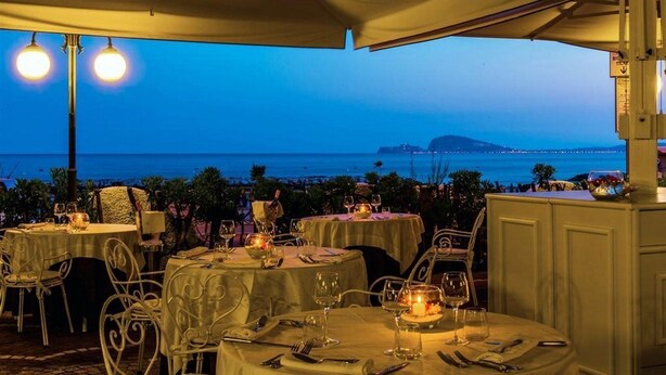 Un espacio de comedor al aire libre con mesas dispuestas para una comida, con vistas a la costa.