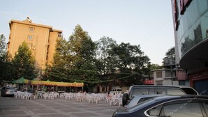 A building with a yellow facade, outdoor seating area with white tables and chairs, and a parked car in front.