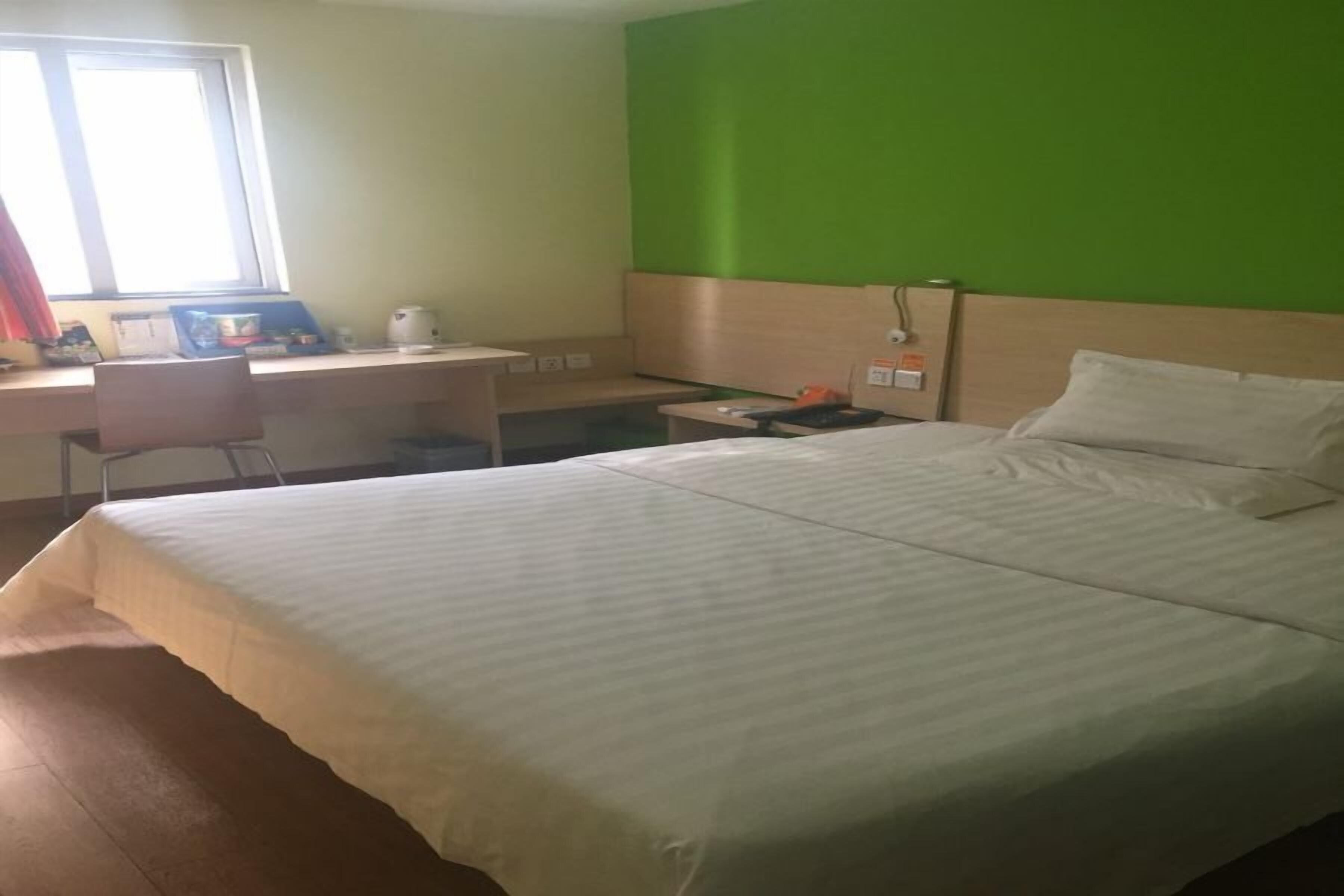 Et hotelværelse med en stor seng, et skrivebord med stol, et lille bord og en grøn accentvæg.