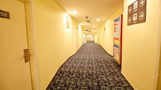 A hotel hallway with a patterned carpet, yellow walls, and numbered doors.