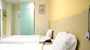 A hotel room with two beds, a wooden headboard, a wall-mounted phone, and a poster.