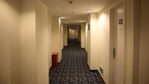 A hotel hallway with carpeted floors, doors on both sides, and a trash bin on the left. - 7 Days Inn (Xiamen)
