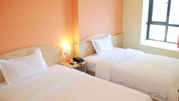 A hotel room with two single beds, a bedside table with a lamp, a phone, and a small table with a bottle. - 7 Days Inn (Xiamen)