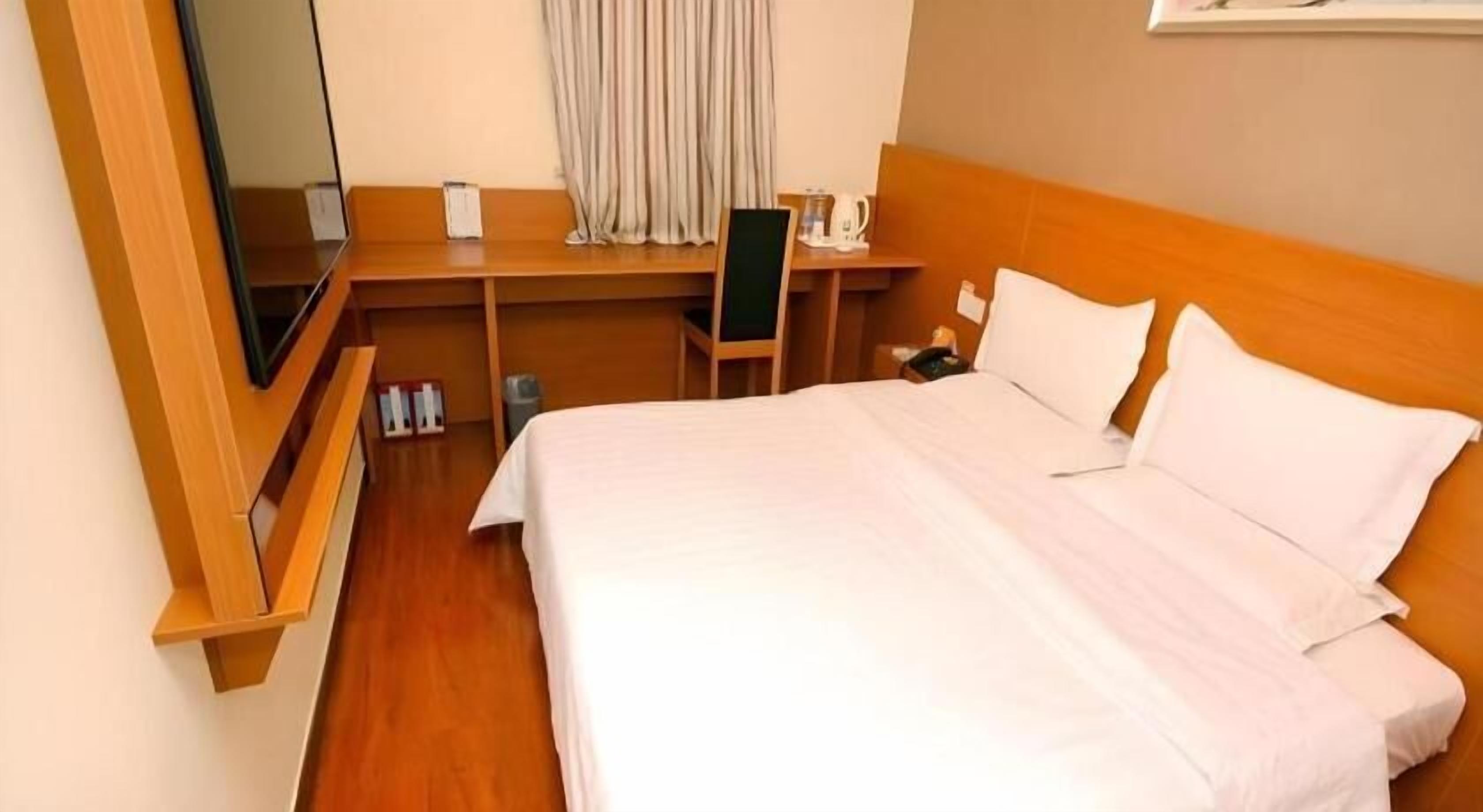 Habitación de hotel con una cama grande, un escritorio, una silla, un televisor y una ventana con cortinas.