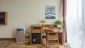 Una camera compatta con angolo cottura, scrivania e sedia. Sulla scrivania si trova un piccolo termosifone, un cestino e una pianta in vaso.