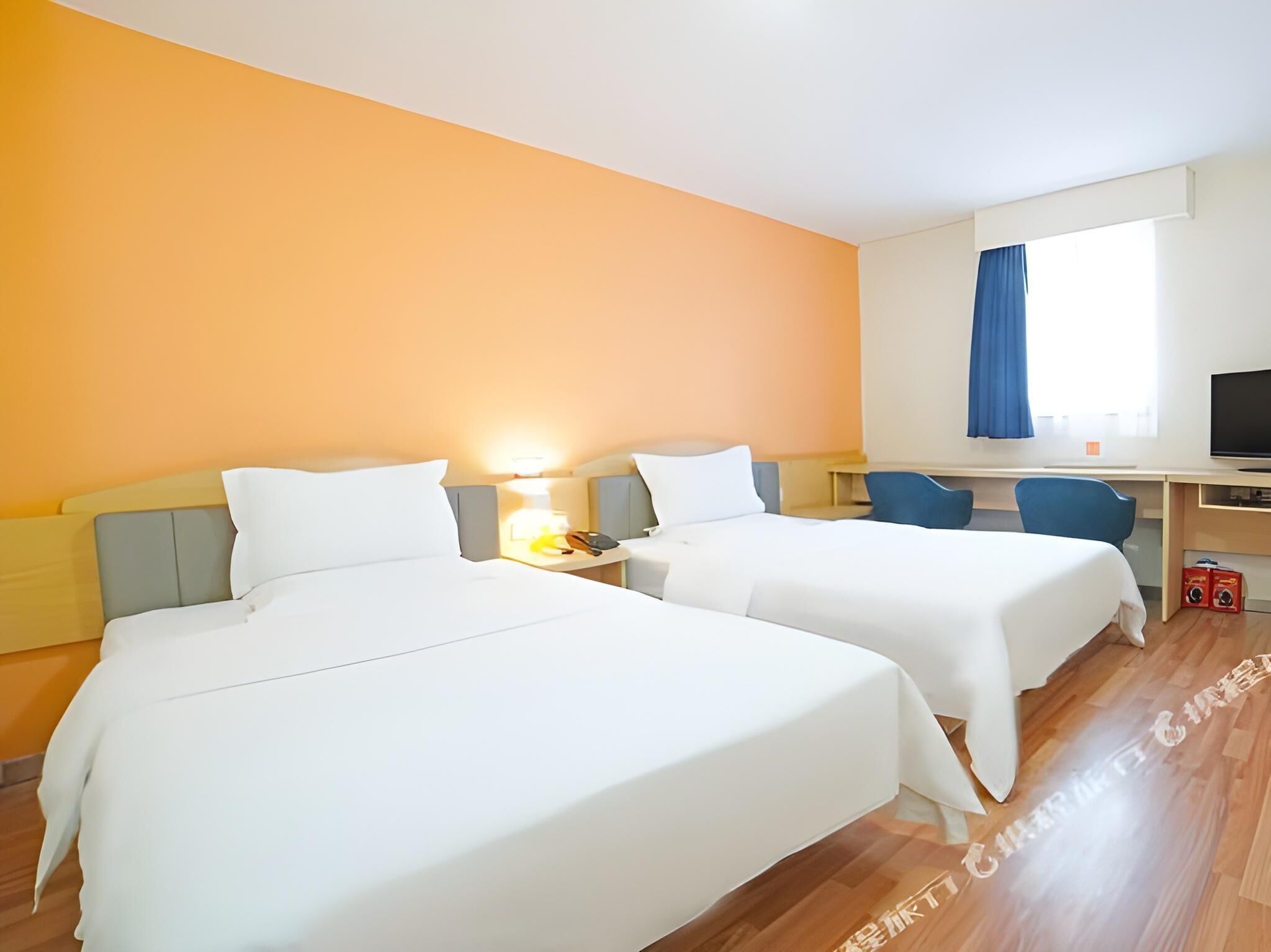 Une chambre d’hôtel avec deux lits, un bureau, une chaise, une télévision et une fenêtre avec des rideaux.