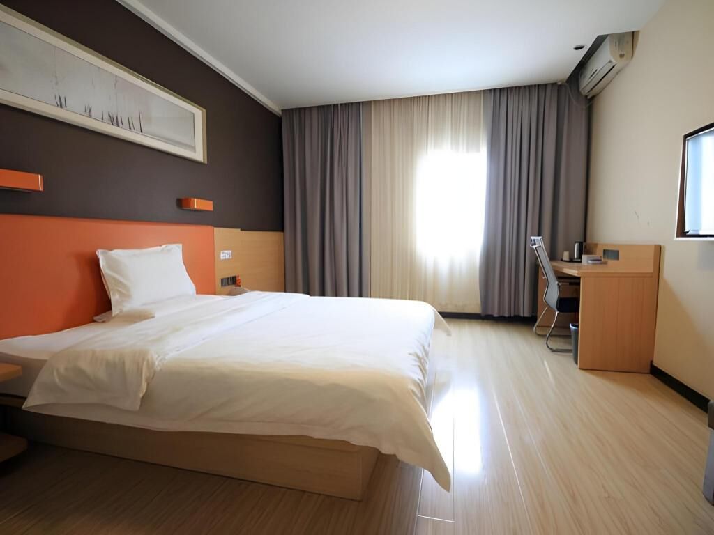 Habitación de hotel con cama, escritorio, silla, ventana con cortinas e imagen enmarcada en la pared.