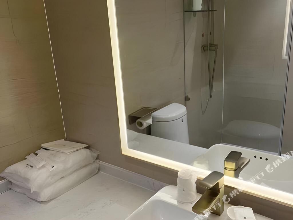 Un baño moderno con un espejo grande, un inodoro y un lavabo con grifo dorado.
