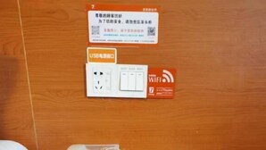 Habitación de hotel con un escritorio de madera, un teléfono blanco, un control remoto, un teléfono móvil y pantuflas en el suelo.