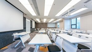 A conference room with white tables and chairs, a projector screen, and a large window with a city view. - 7 Days Inn (Nanchang)