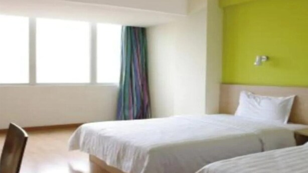 A hotel room with two beds, a window with curtains, and a green accent wall. - 7 Days Inn (Nanchang)