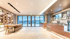 A modern hotel lobby with a reception desk, a seating area with a wooden table and chairs, and a large window offering a view of the outside. - 7 Days Inn (Nanchang)