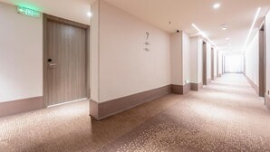 A long, well-lit hallway with a carpeted floor, a door with a number, and a green exit sign. - 7 Days Inn (Nanchang)