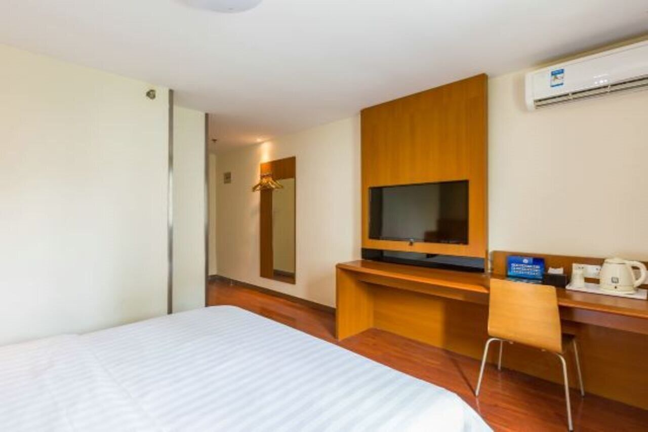 Habitación de hotel con cama, escritorio con silla, televisión y aire acondicionado.