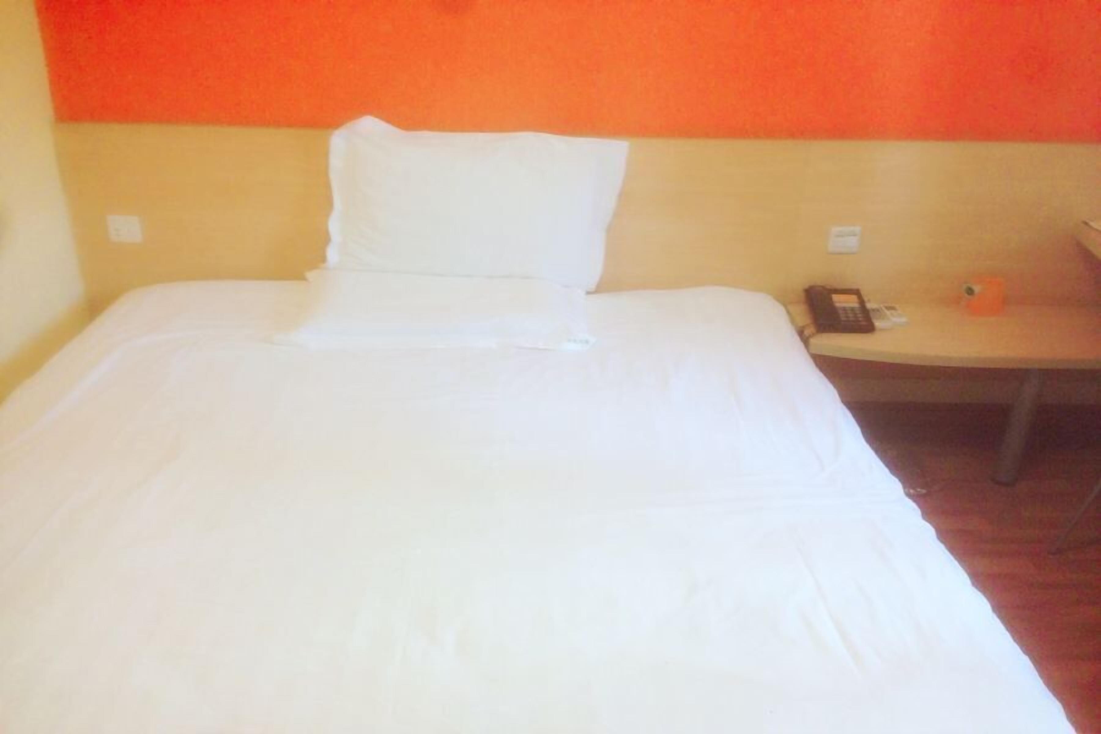 A hotel room with a large bed, a bedside table with a phone, and a small orange object on the table.