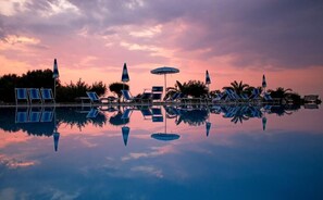 A poolside area with lounge chairs and umbrellas, surrounded by trees and a clear sky. - Agriturismo Ninea (Ricadi)