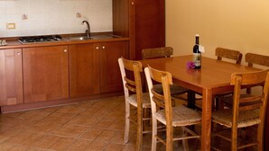 A kitchen with wooden cabinets, a tiled backsplash, a gas stove, and a dining table with chairs. - Agriturismo Ninea (Ricadi)