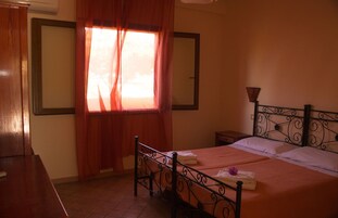 Une chambre à coucher avec un lit, une table de chevet, une commode en bois, une fenêtre avec des rideaux et un miroir au mur.