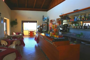 A restaurant with tables, chairs, a bar area with bottles, and a television. - Agriturismo Ninea (Ricadi)