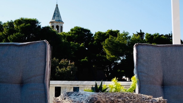 Vista de una aguja de iglesia con una cruz en la cima, rodeada de árboles verdes y frondosos.