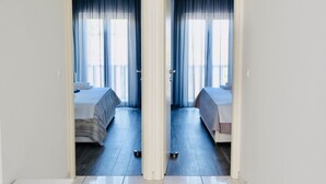 Habitación de hotel con dos camas, un ventanal con cortinas azules y una puerta blanca.