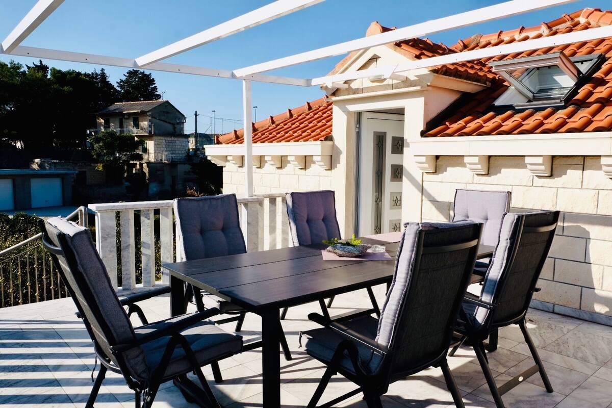 Un patio al aire libre con una mesa y sillas, piso de baldosas y un edificio con techo de tejas al fondo.