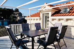 Un patio al aire libre con una mesa y sillas, una pérgola y vistas a un edificio con tejado de tejas.
