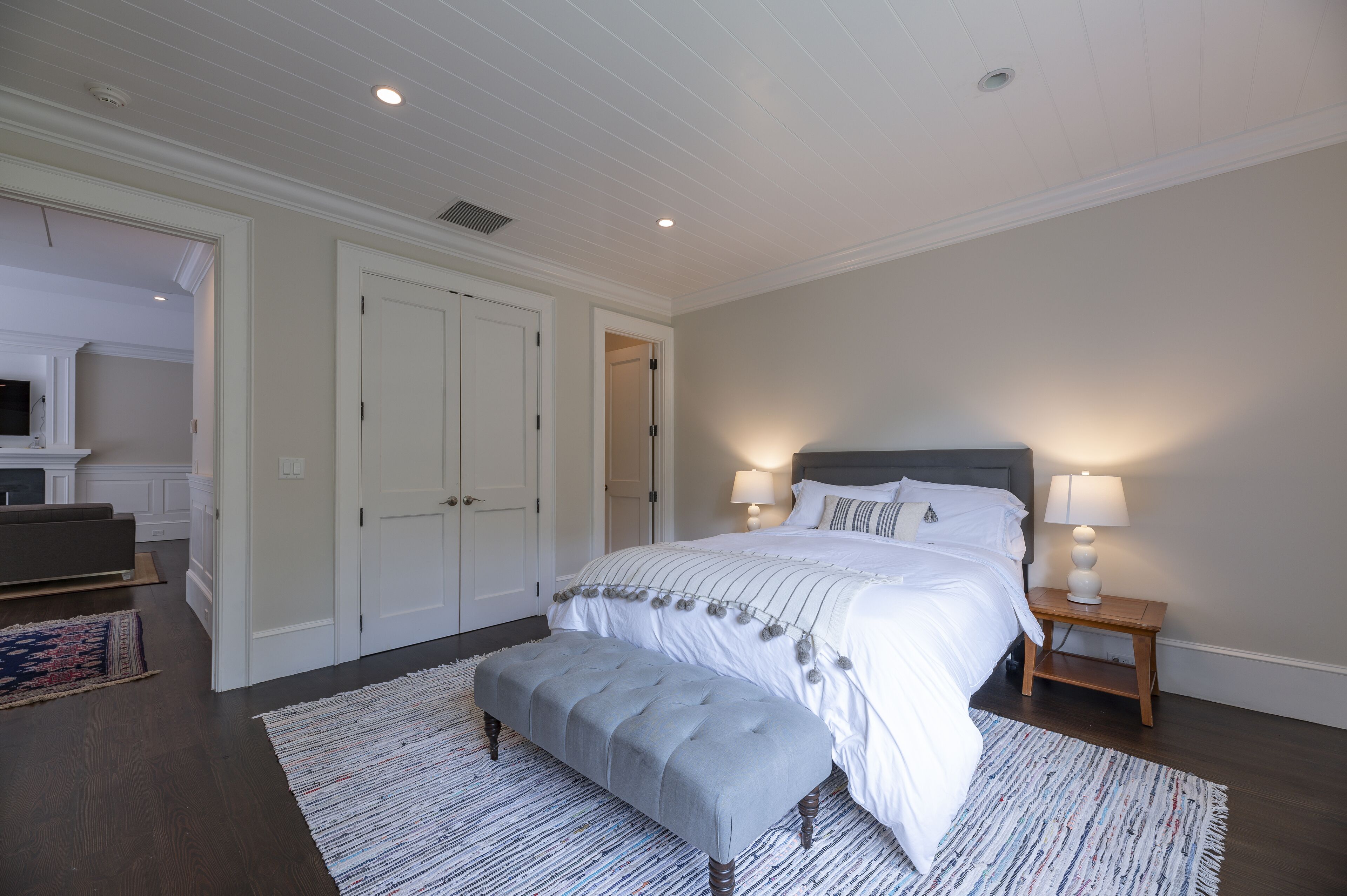A bedroom with a large bed, a bench, two nightstands, and a television in the corner.