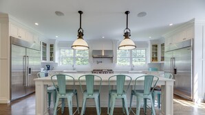 A kitchen with white cabinets, stainless steel appliances, a central island with chairs, and pendant lighting. - Mansion Near the Bay. 7 bedrooms! Chef’s kitchen. (Southampton)