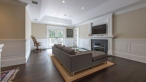 A spacious living room with a sectional sofa, a fireplace, and a television mounted above it. - Mansion Near the Bay. 7 bedrooms! Chef’s kitchen. (Southampton)