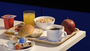 Een dienblad met ontbijtartikelen, zoals brood, boter, jam, een drankje en een appel.