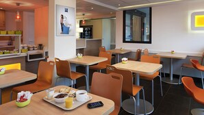 Een moderne eethoek met tafels en stoelen, een keuken op de achtergrond en een groot raam.
