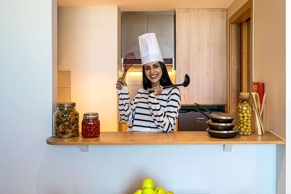A kitchen with a person holding a ladle, jars of preserved food, and a bowl of apples.