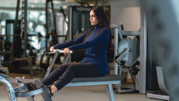 Una persona usando una máquina de remo en un gimnasio con varios equipos de ejercicio al fondo.