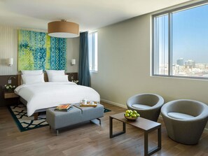 A hotel room with a bed, two armchairs, a small table, a view of the city, and a large window. - Adagio Jeddah City Center (Jeddah)