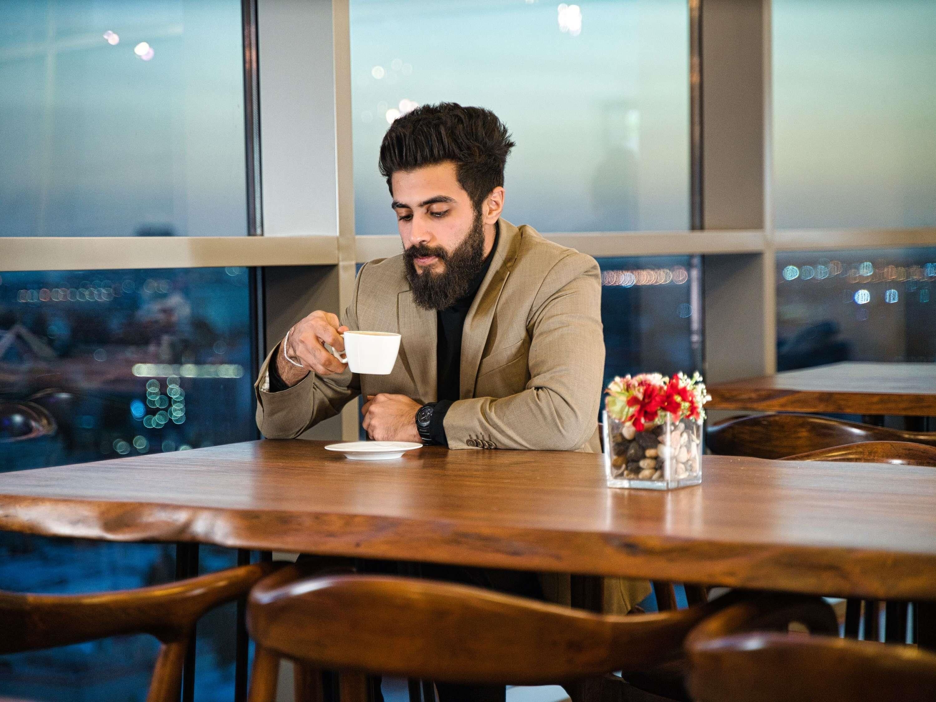 A person seated at a wooden table in a cafe with a view of the cityscape through large windows.