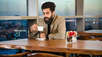 A person seated at a wooden table in a cafe with a view of the cityscape through large windows.