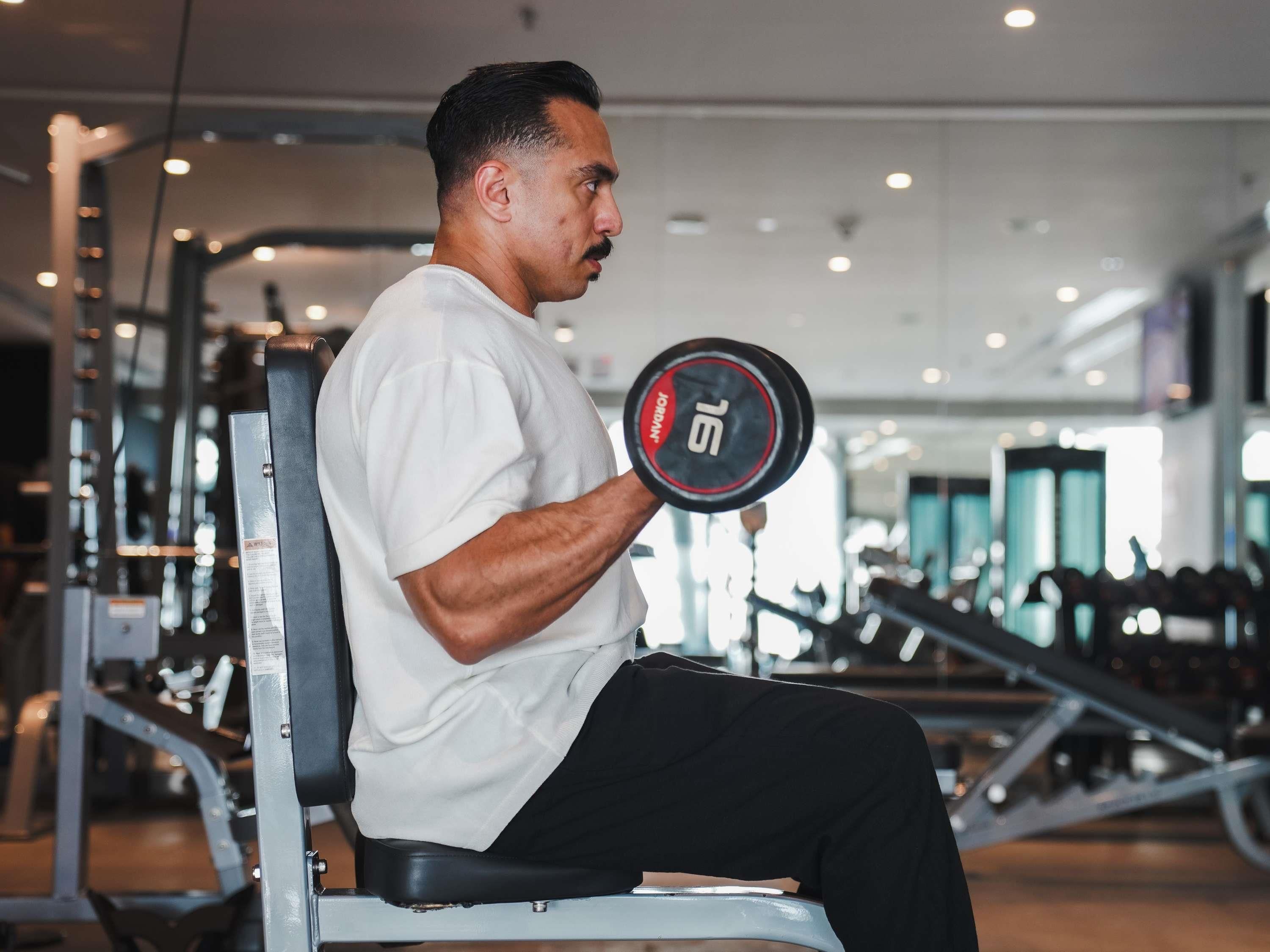 A person seated on a gym machine, holding a dumbbell with the number 15.