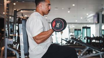 A person seated on a gym machine, holding a dumbbell with the number 15.