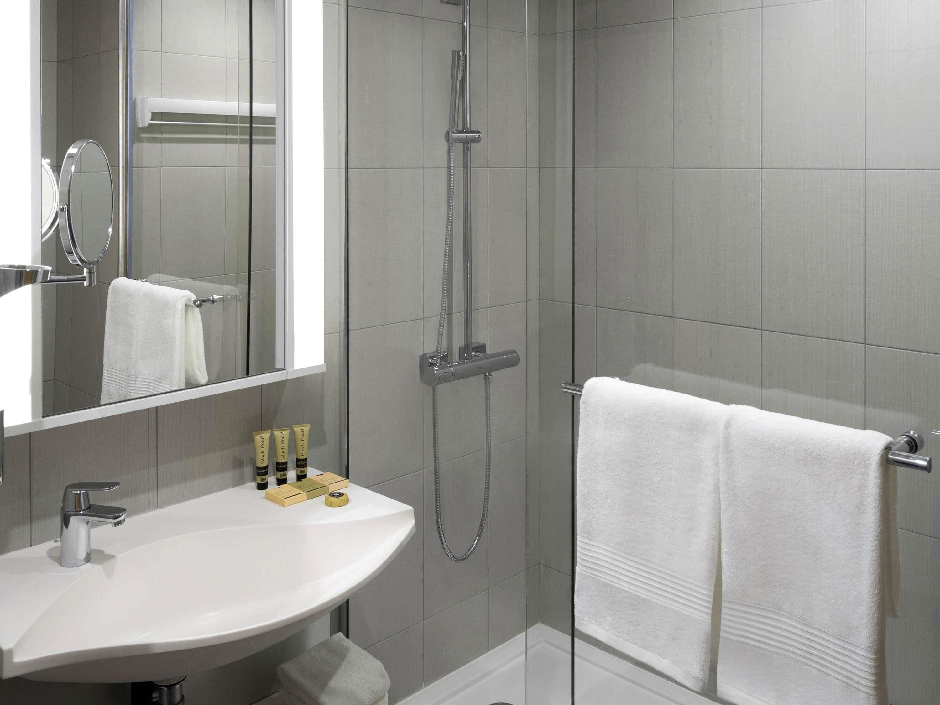 A modern bathroom with a white sink, a mirror, a shower, and two white towels.
