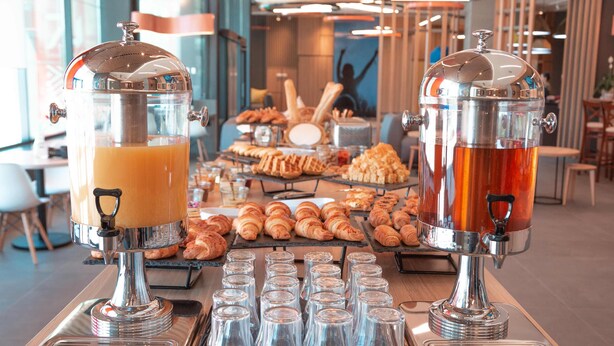 Een buffetopstelling met twee drankdispensers, diverse gebakjes en verschillende lege glazen op een tafel.