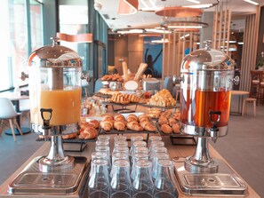 A buffet setup with two beverage dispensers, a variety of pastries, and several empty glasses on a table.