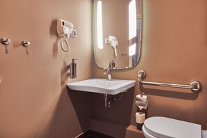 A bathroom with a sink, mirror, hairdryer, toilet, and grab bar.